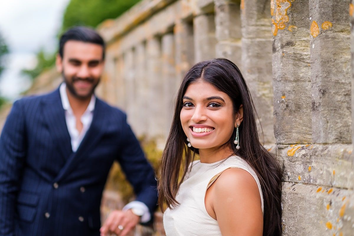 A romantic wedding couple poses against a stone wall backdrop at an elegant venue.