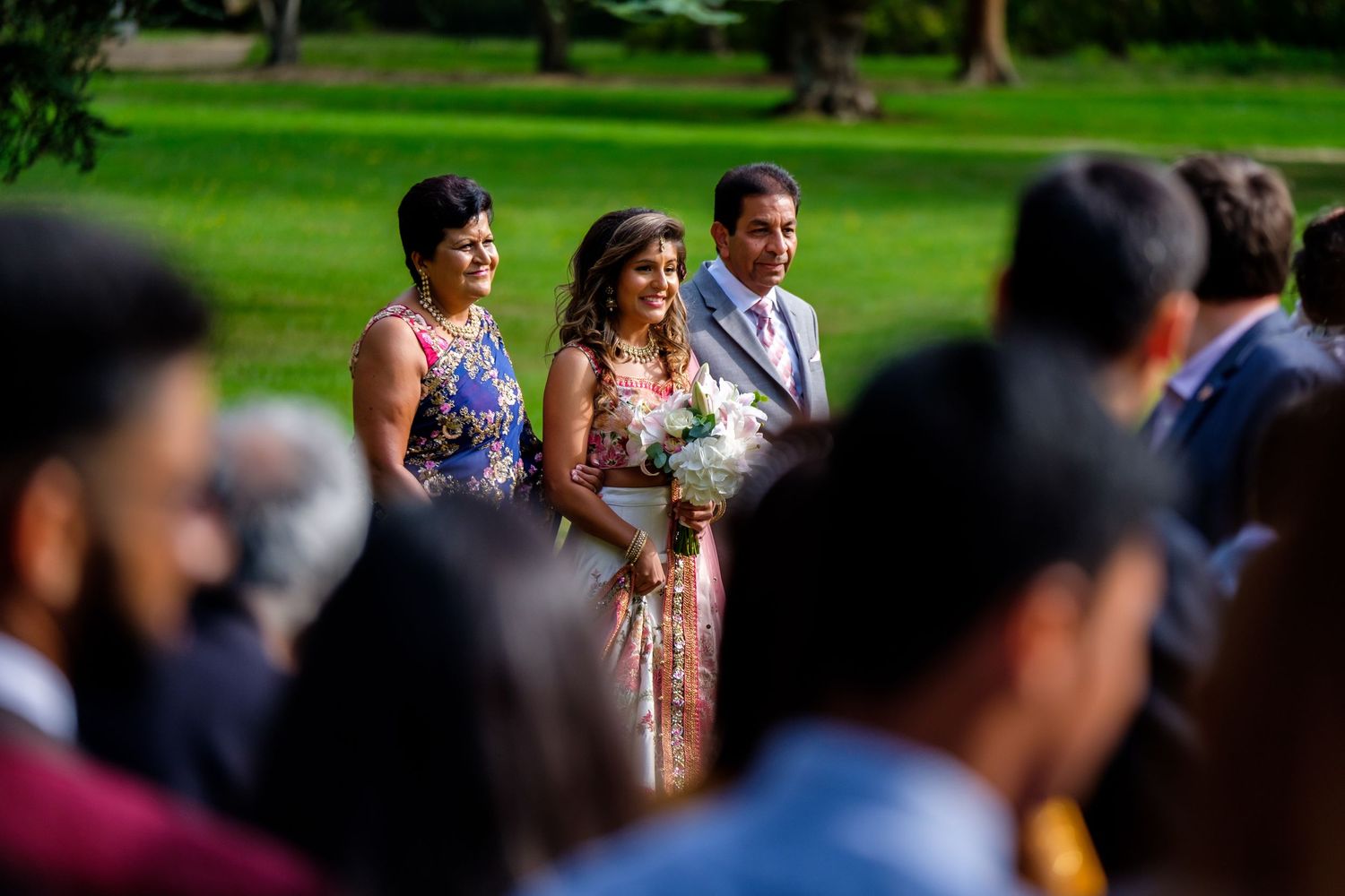 Wedding guests seated outdoors in a formal garden setting during a summer ceremony.