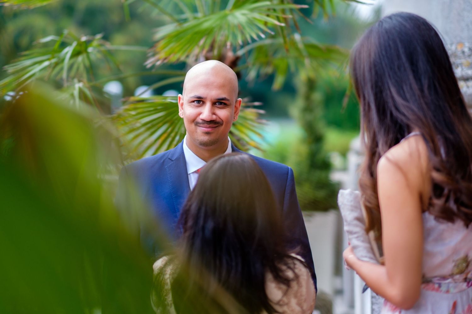 A wedding ceremony takes place outdoors with greenery and palm fronds in the background.