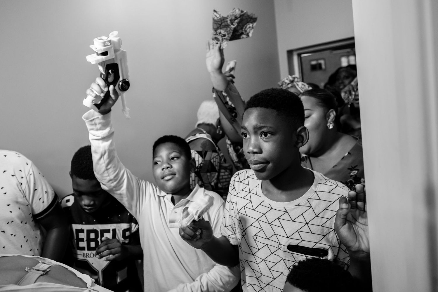Black and white image of a group raising their hands in celebration indoors.