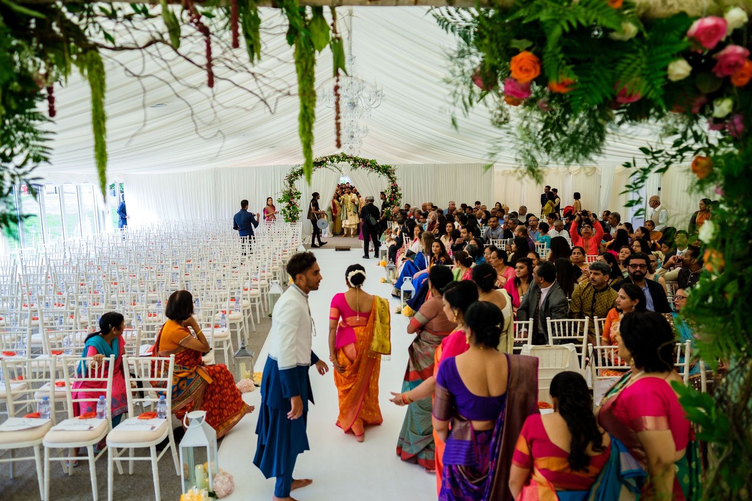 Wedding ceremony setup in a white tent decorated with colorful floral arrangements and greenery.