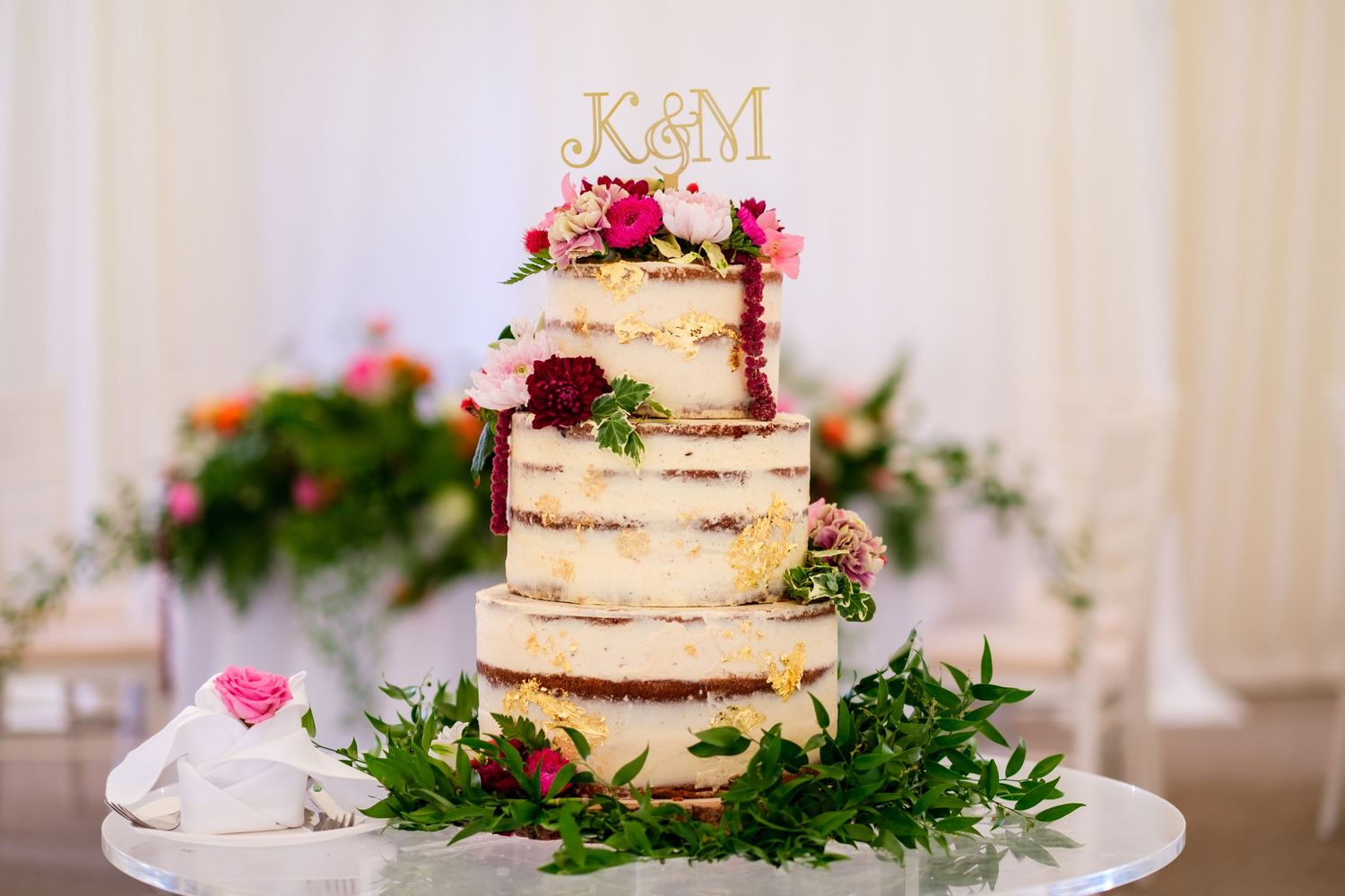 Semi-naked wedding cake decorated with fresh flowers and greenery on display at reception.