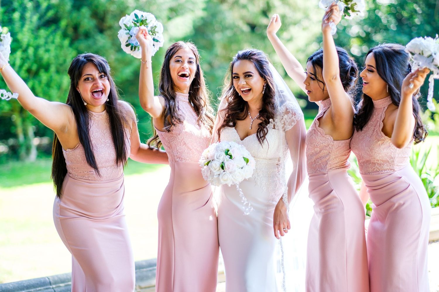 Bridesmaids in pink dresses celebrating joyfully outdoors.