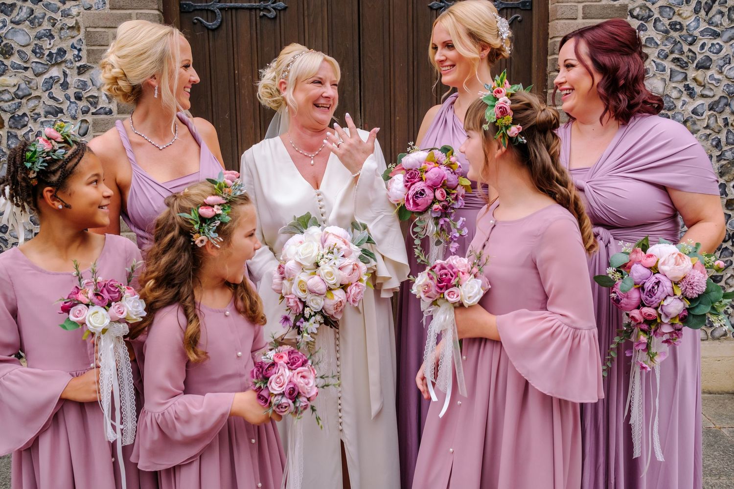 Bridesmaids in dusty rose dresses gather with bouquets of pink and white flowers.