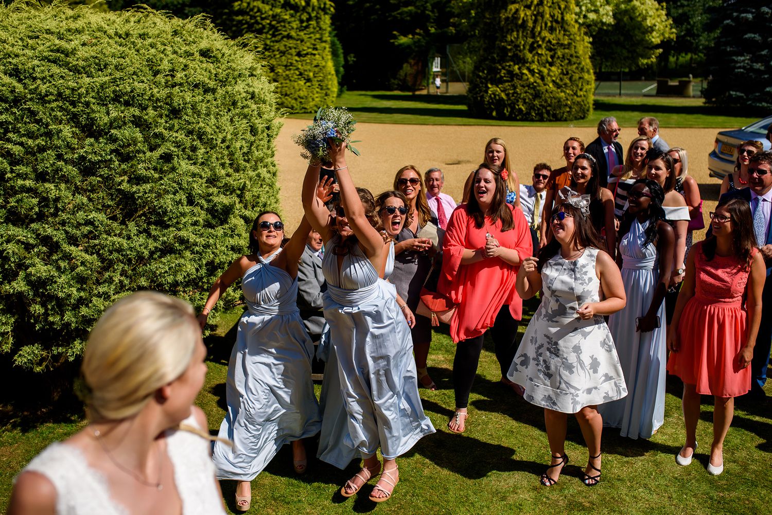 Wedding party and guests assembled on grass for group photographs.