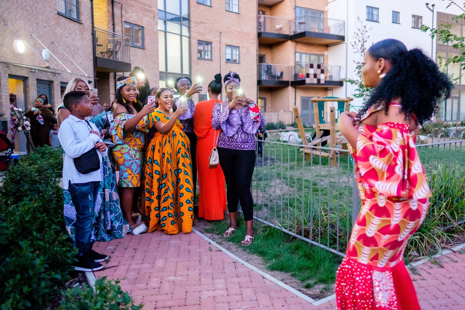 Outdoor community event with people gathered on brick pathways near apartment buildings.