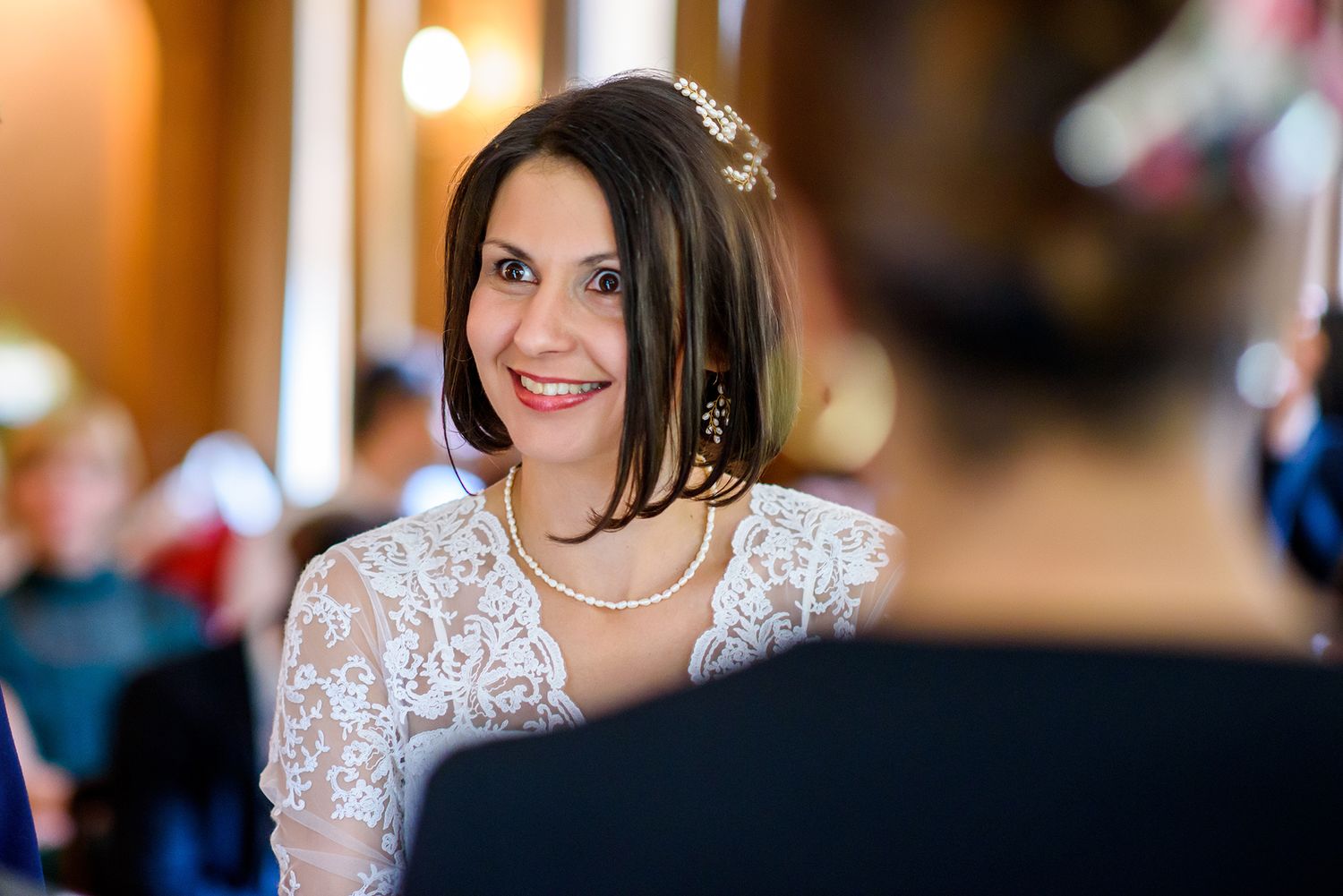 Bride smiles radiantly in delicate lace wedding dress during reception.