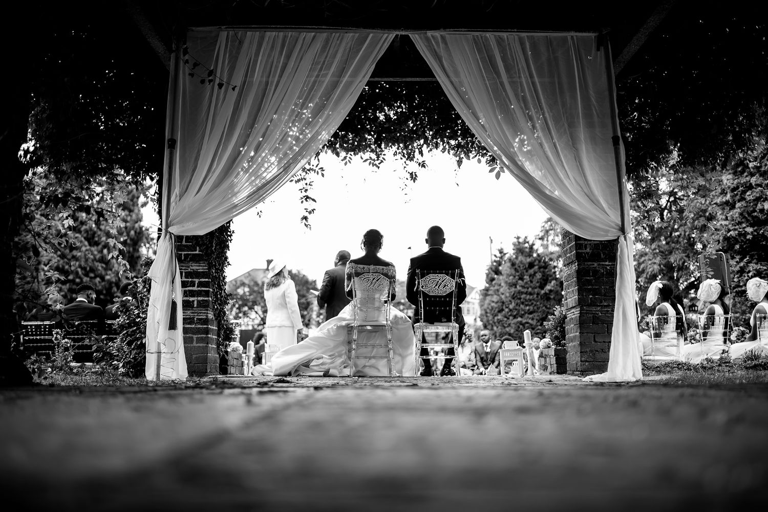 Wedding celebration silhouettes gathered under elegant draped curtains during an outdoor ceremony.