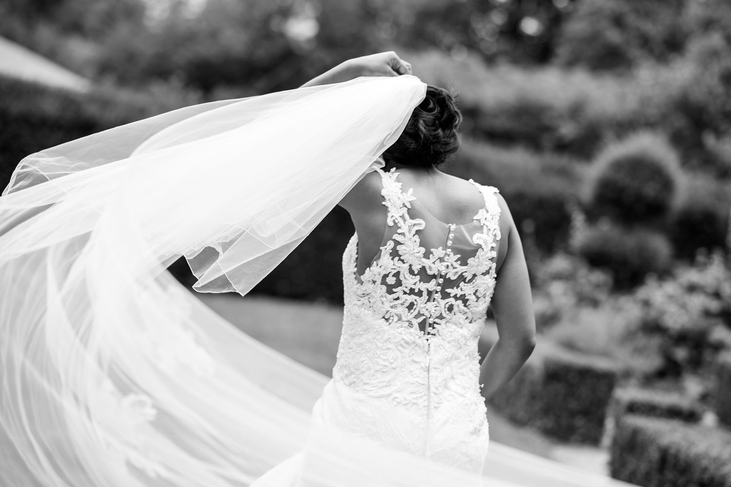 Flowing white wedding veil and dress fabric billows in the wind against a natural outdoor backdrop.