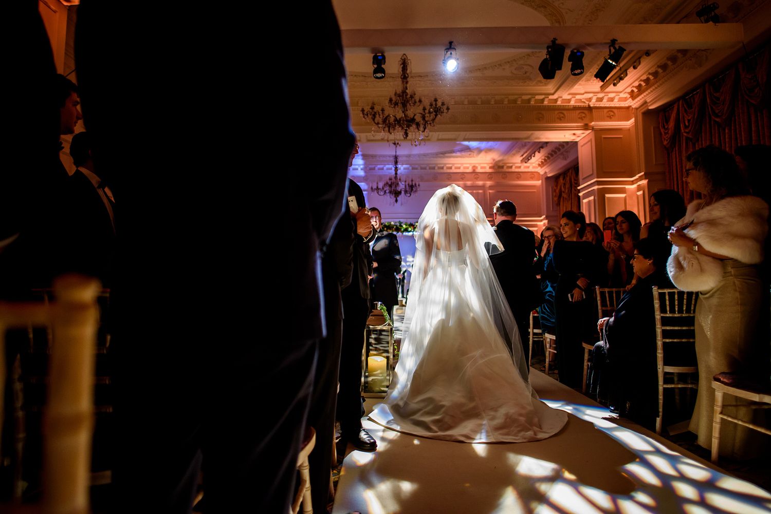 Romantic ballroom wedding ceremony captured in dramatic silhouette lighting.