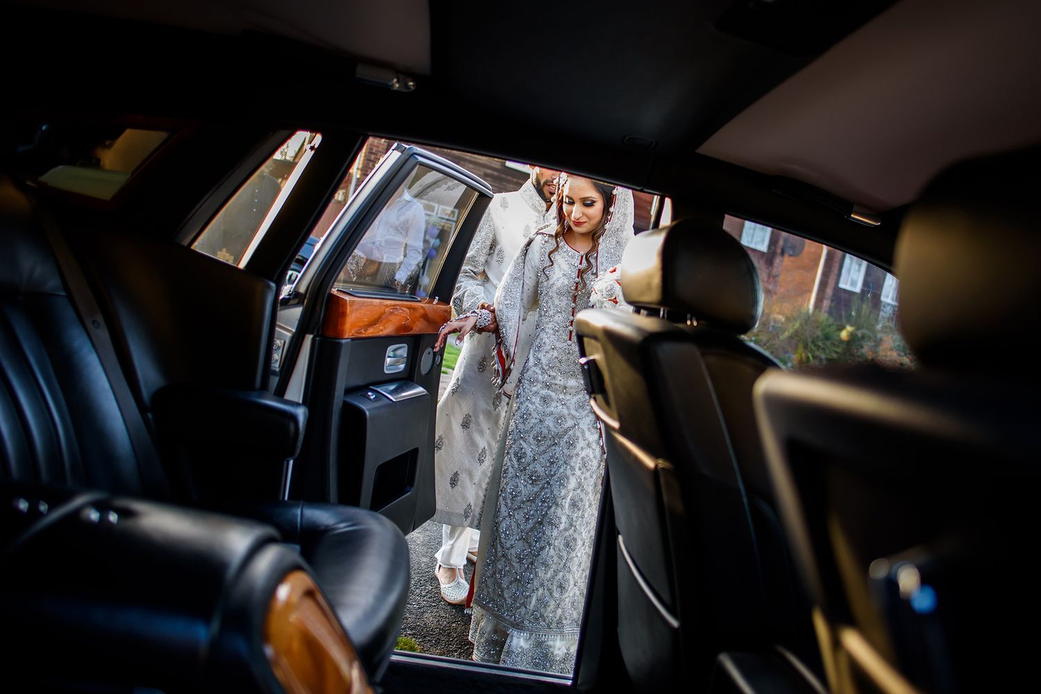 Bridal couple sits in elegant wedding attire inside a luxury vehicle.