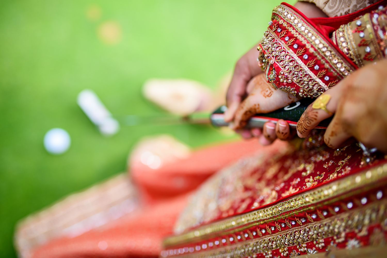 Close-up detail of hands adorned with traditional bridal mehndi and jewelry against a green background.