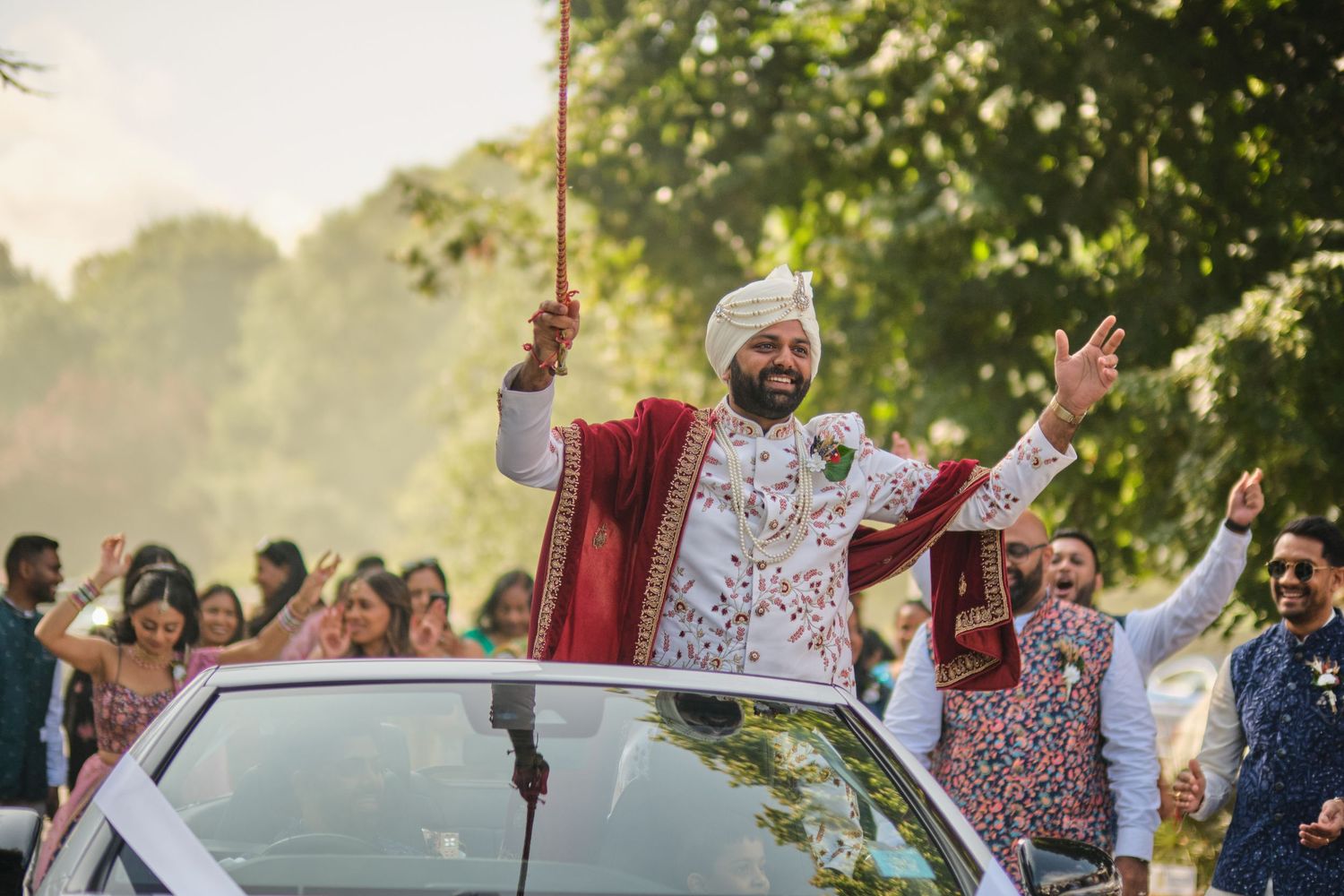 Joyful wedding procession with traditional baraat ceremony taking place outdoors in natural sunlit setting.