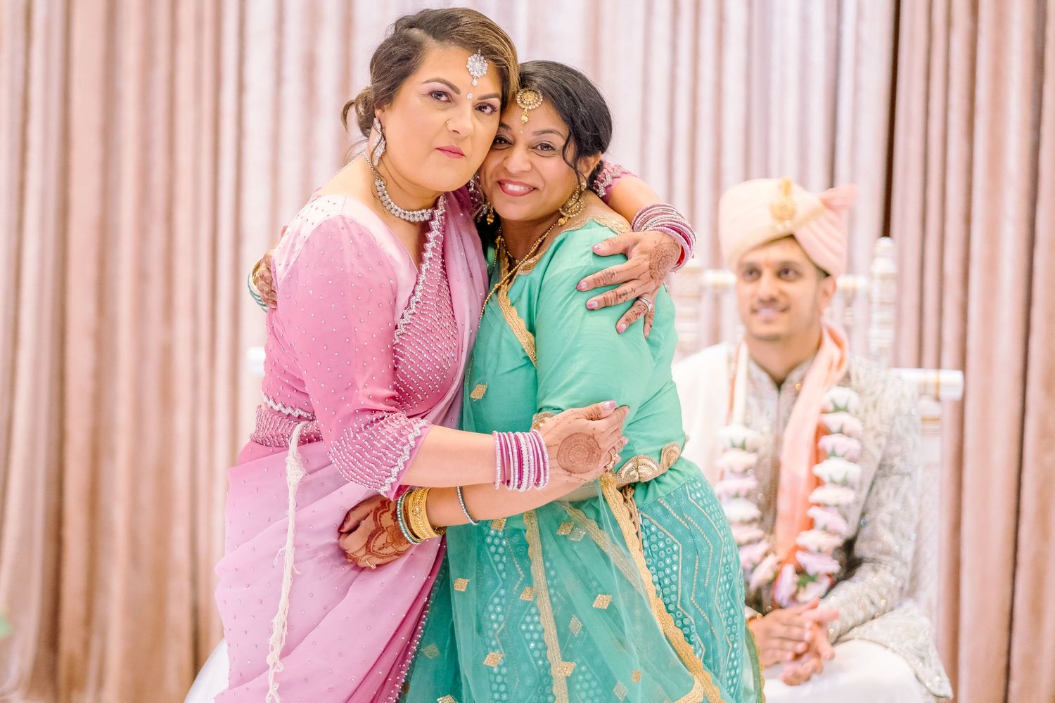 Wedding party members in turquoise and pink attire embracing during celebrations.