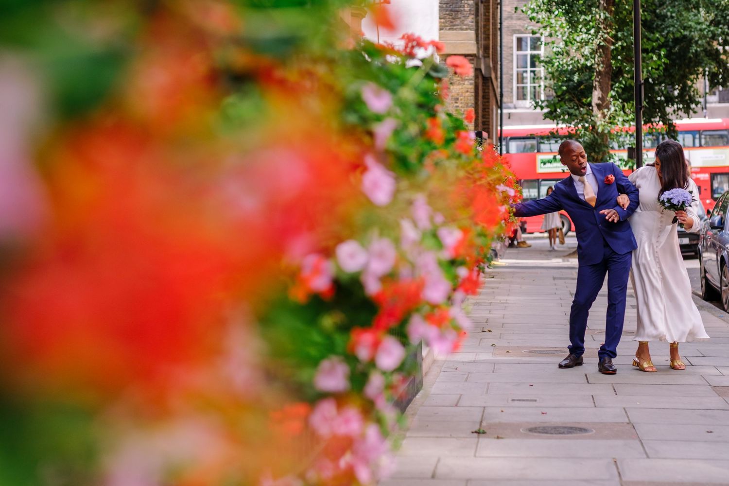 A couple dancing joyfully on a street with vibrant red flowers in the foreground.