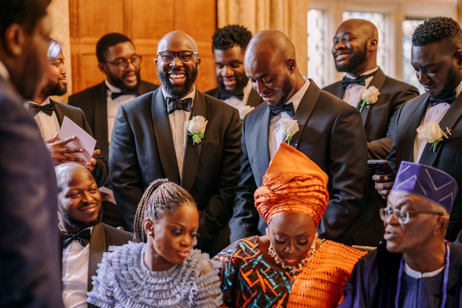 A joyful group celebrates at an indoor event with bright orange traditional attire and formal wear.