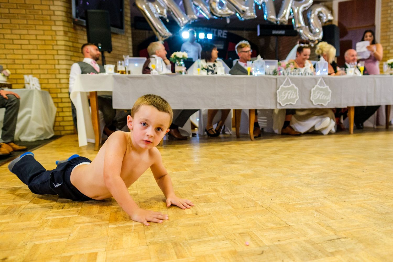 Wedding guests dance and celebrate on a polished wooden dance floor at a reception.