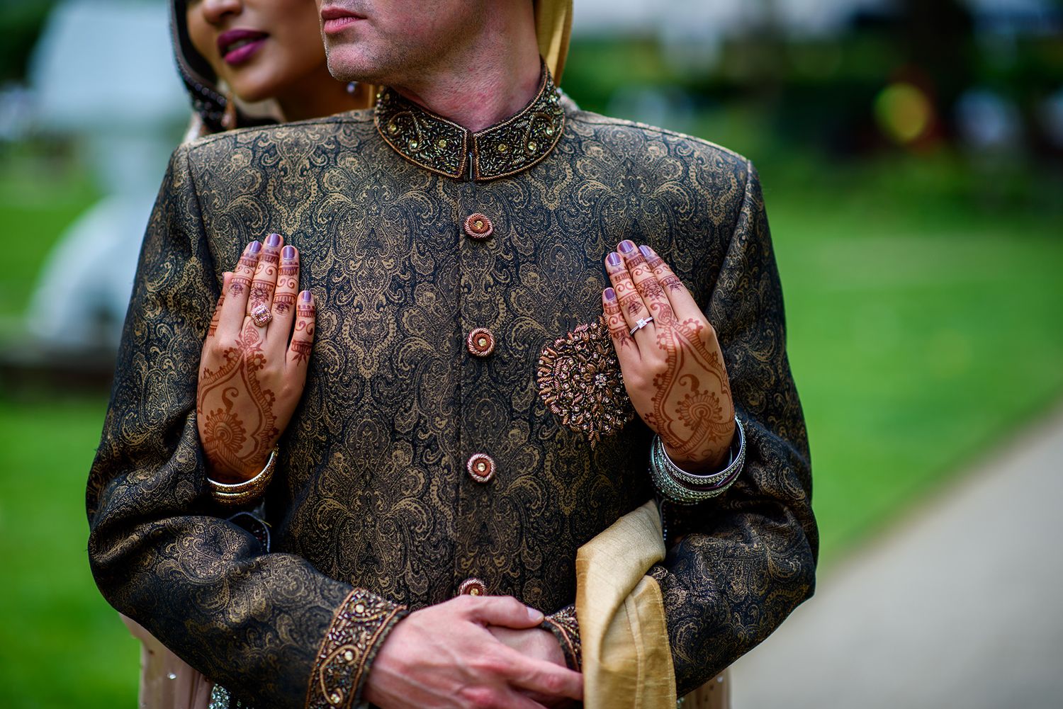 Traditional South Asian groom wearing embroidered sherwani suit poses outdoors.
