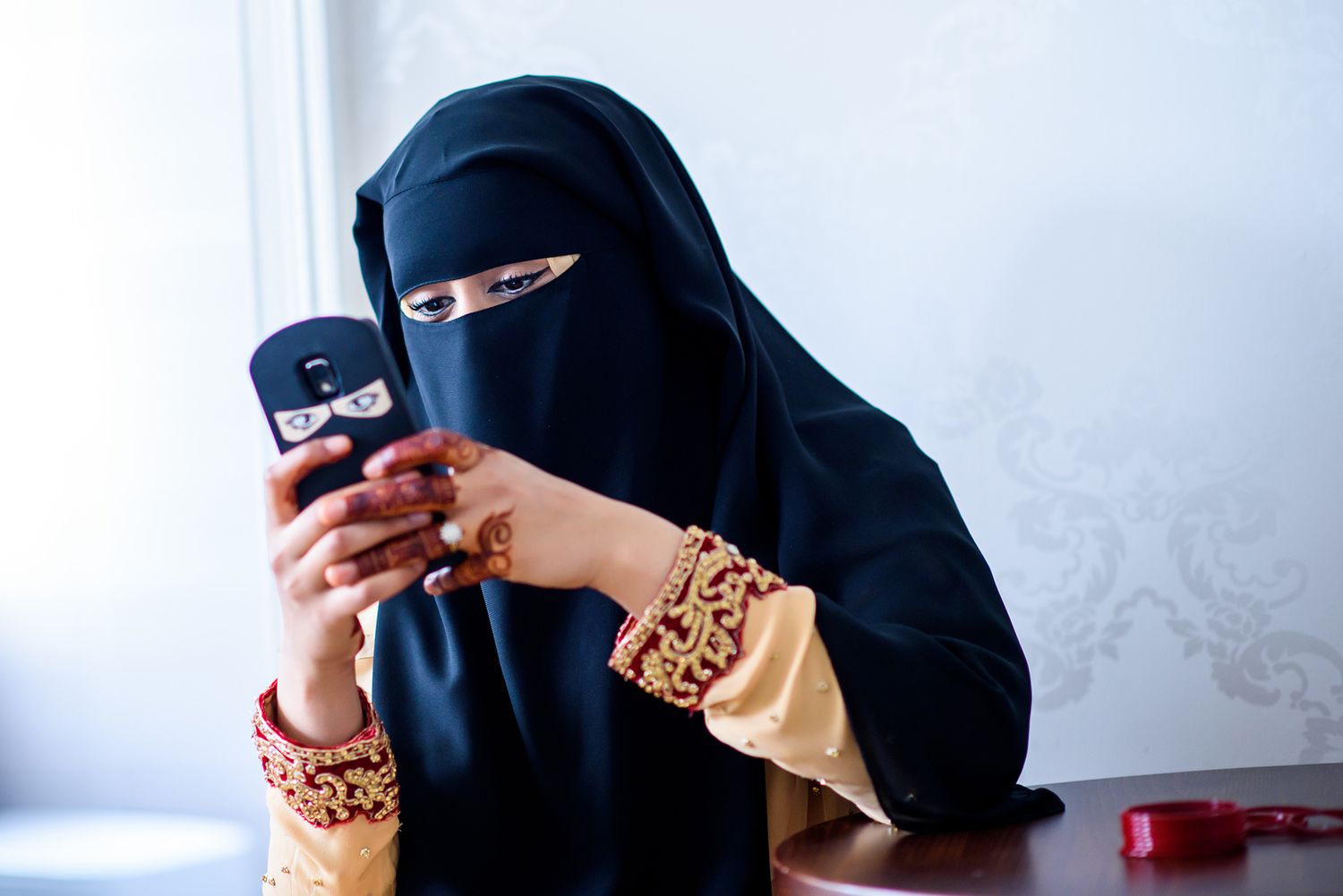 Woman in black hijab using mobile phone while holding a beverage.