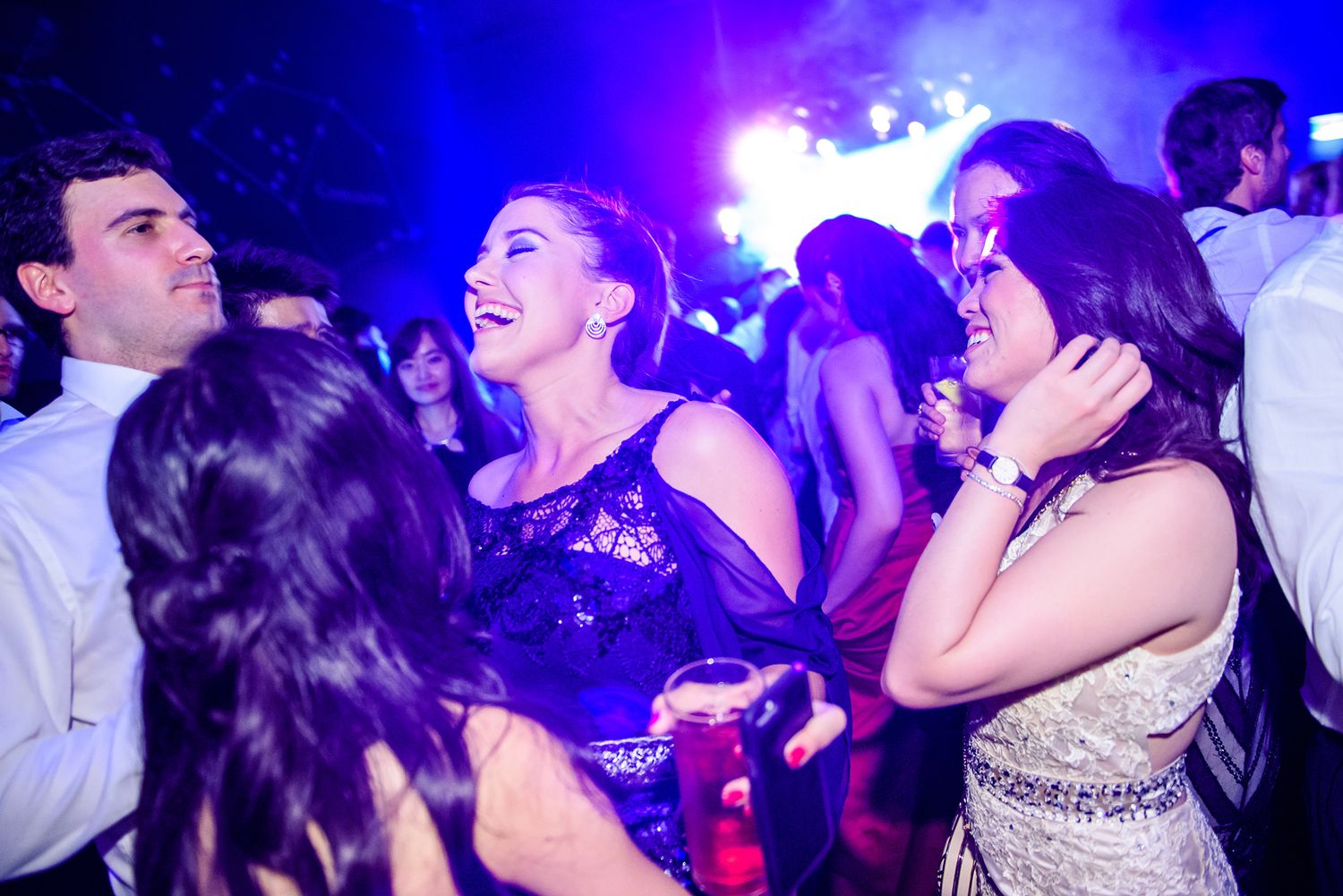 Crowd dancing in a nightclub with purple and blue lighting creating an energetic party atmosphere.