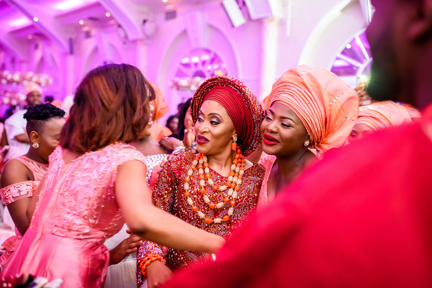 Wedding party celebrating on dance floor bathed in vibrant pink and purple lighting.