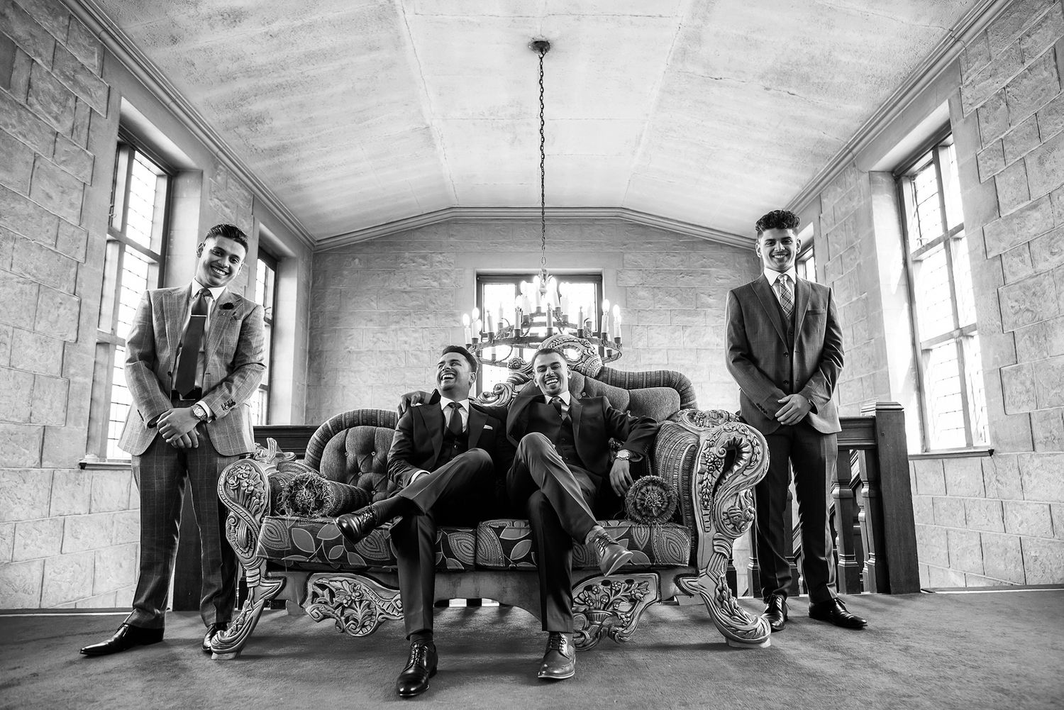 Formal black and white photo of three people posed on vintage furniture in an elegant room.