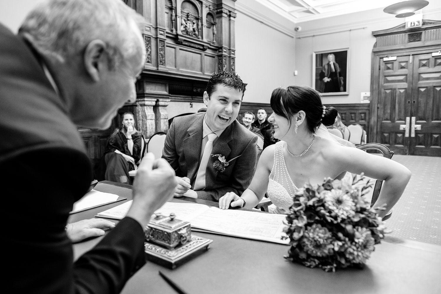 Wedding party signing documents in formal setting with floral arrangements.