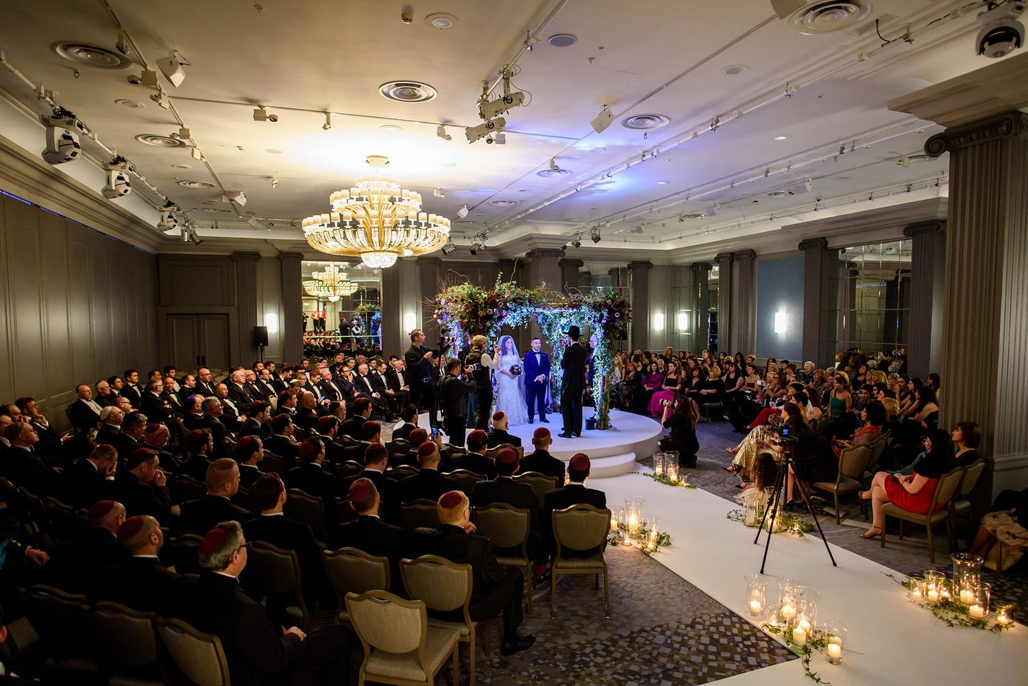Wide view of wedding ceremony in an elegant ballroom with seated guests and center aisle.