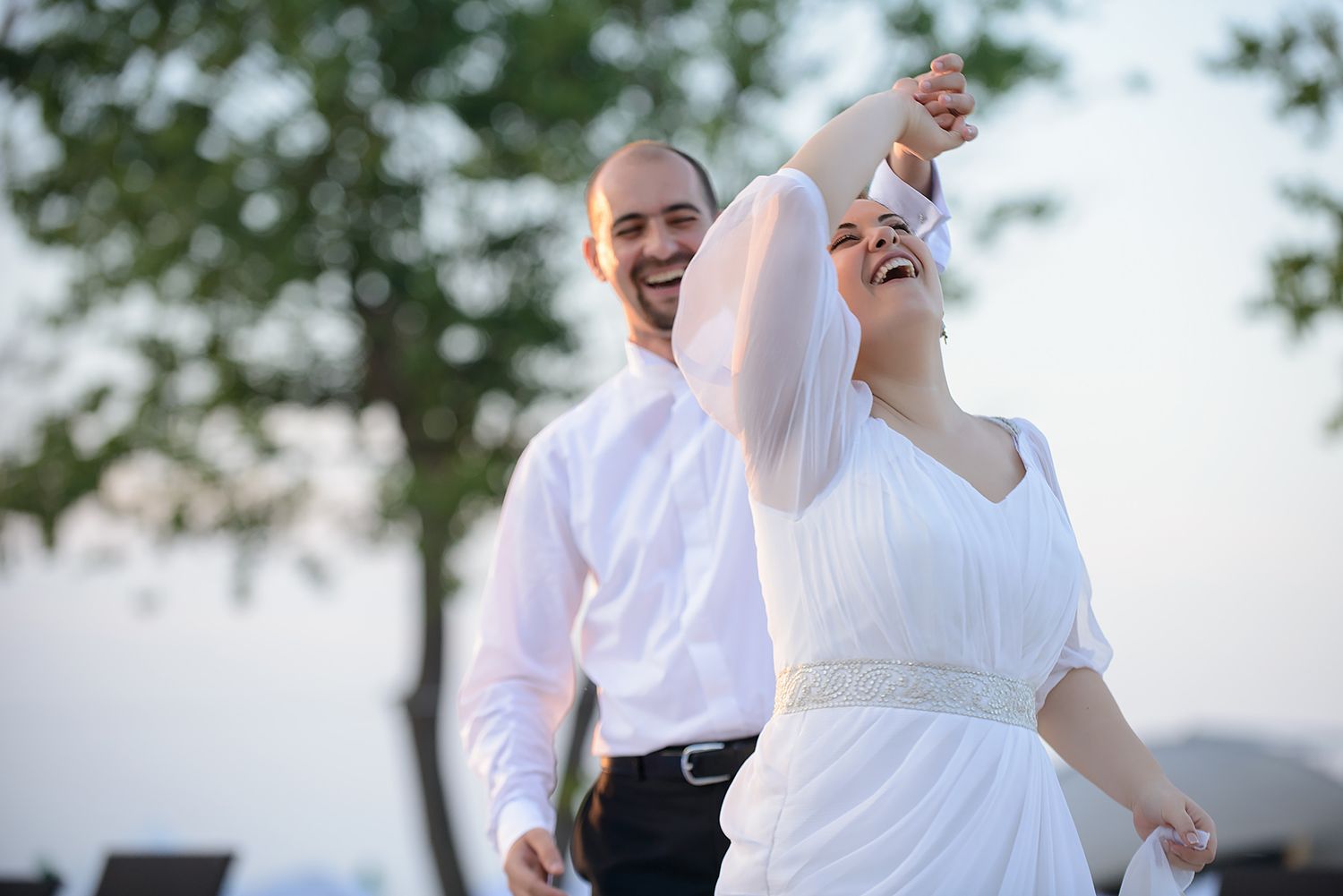 A couple dancing outdoors in formal wedding attire at sunset.