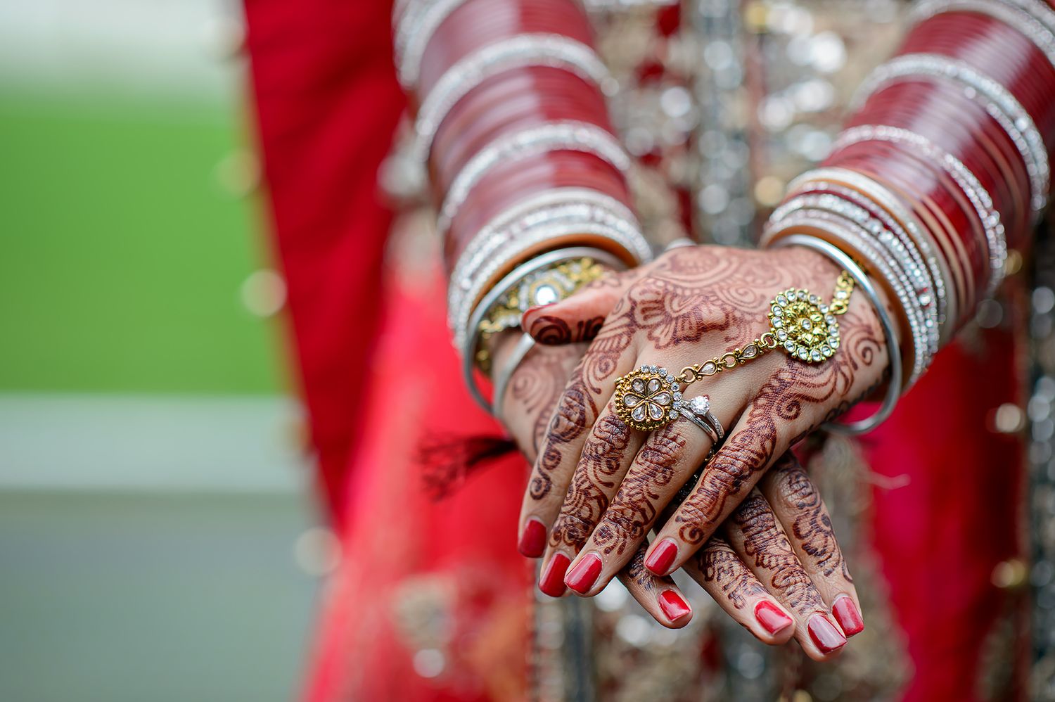 Close-up of hands adorned with traditional mehndi designs and bangles against green background.