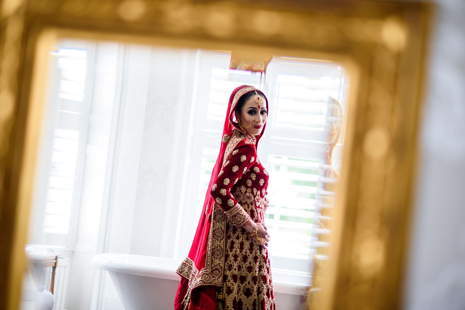 Artistic portrait through golden mirror frame in natural window light.