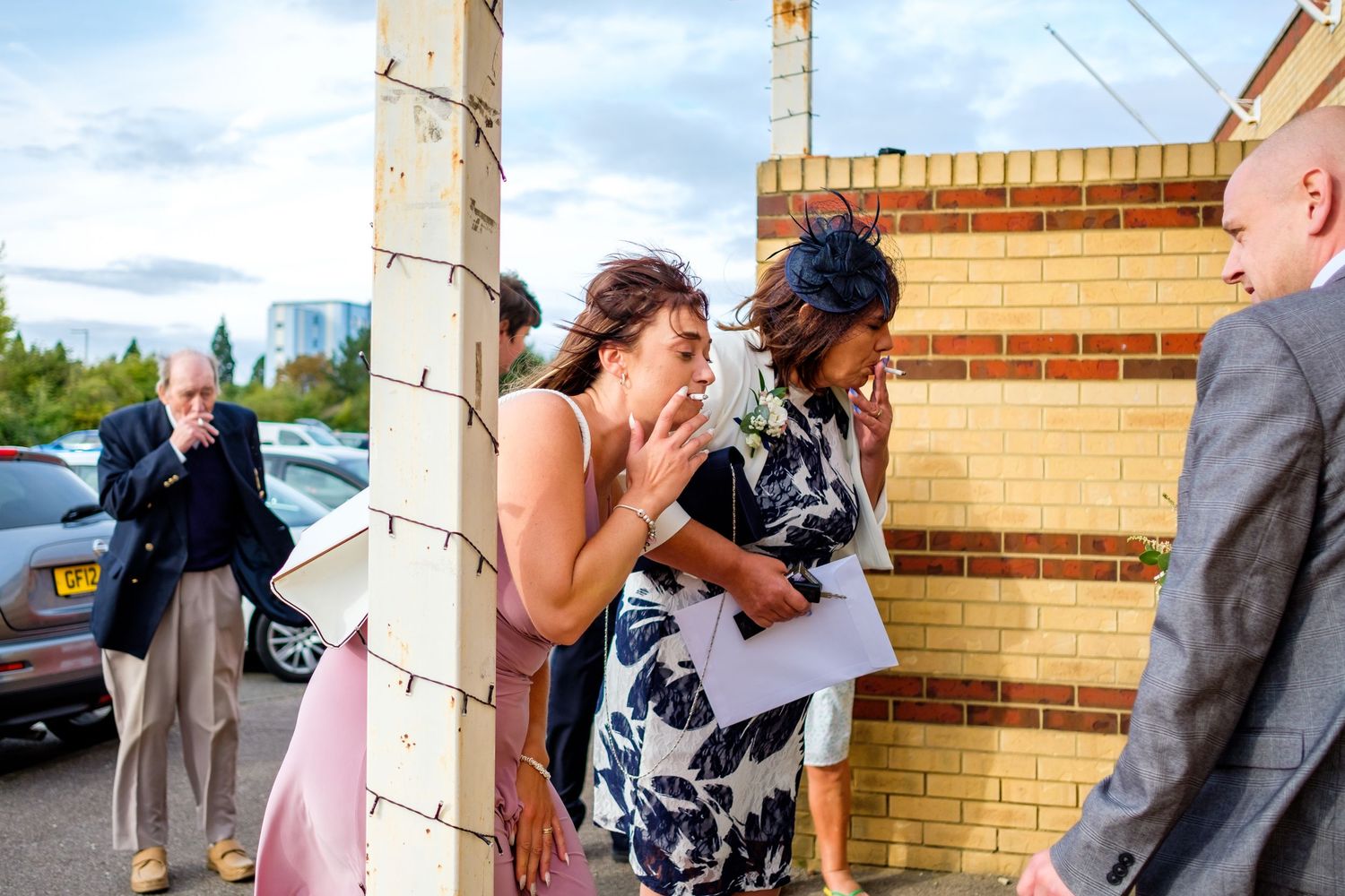 Wedding guests mingling outside a brick building on a bright summer day.