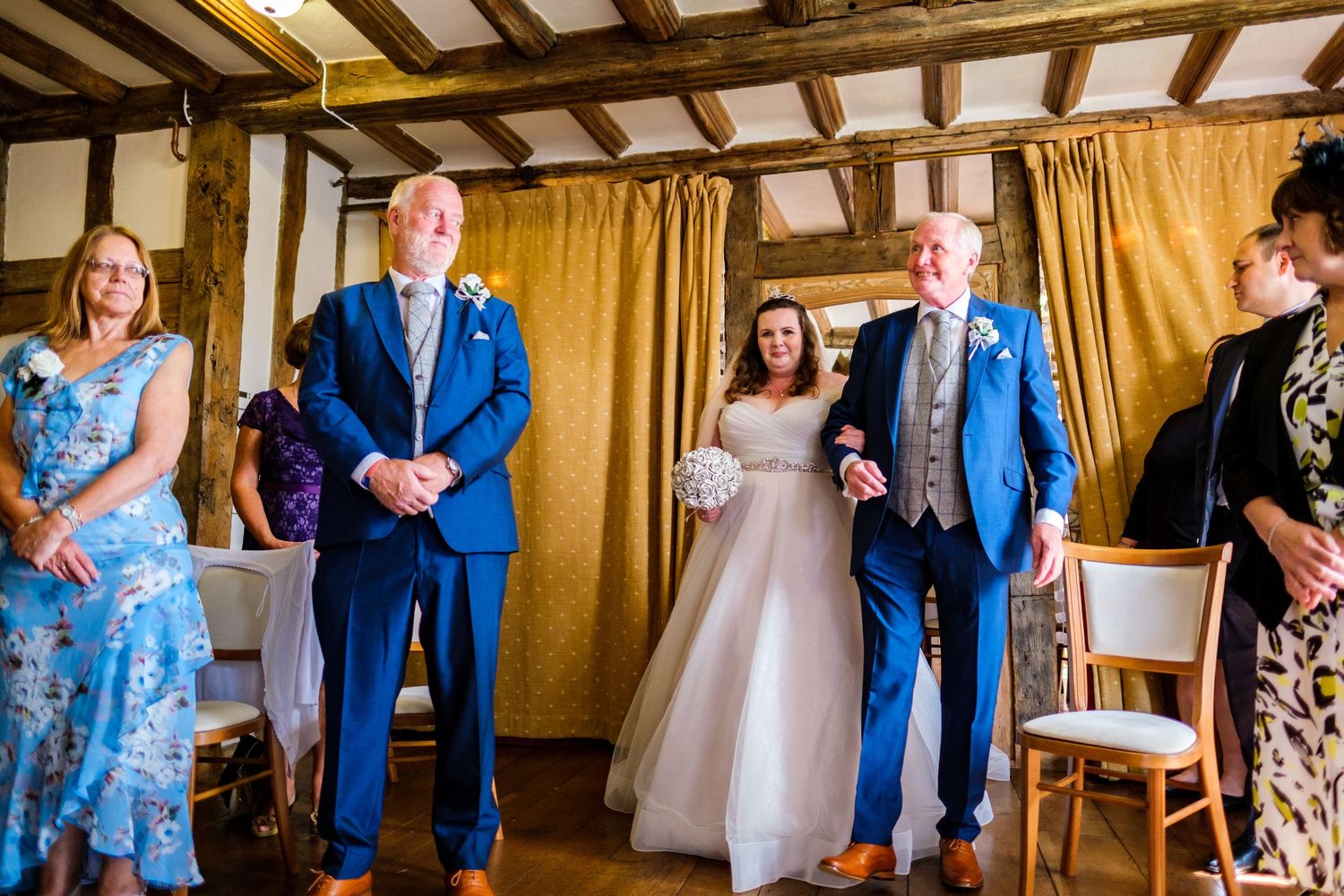 Wedding guests celebrate at a rustic venue with golden curtains and wooden beams.