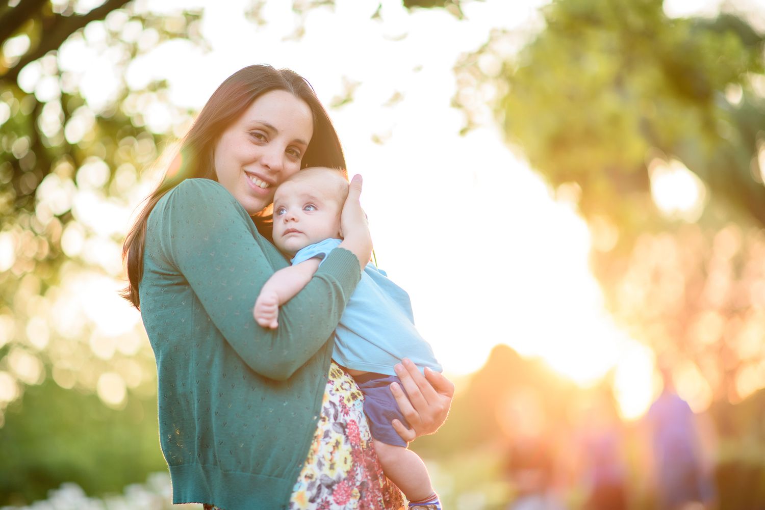 A family embraces in a sunlit outdoor setting with golden light filtering through trees in the background.