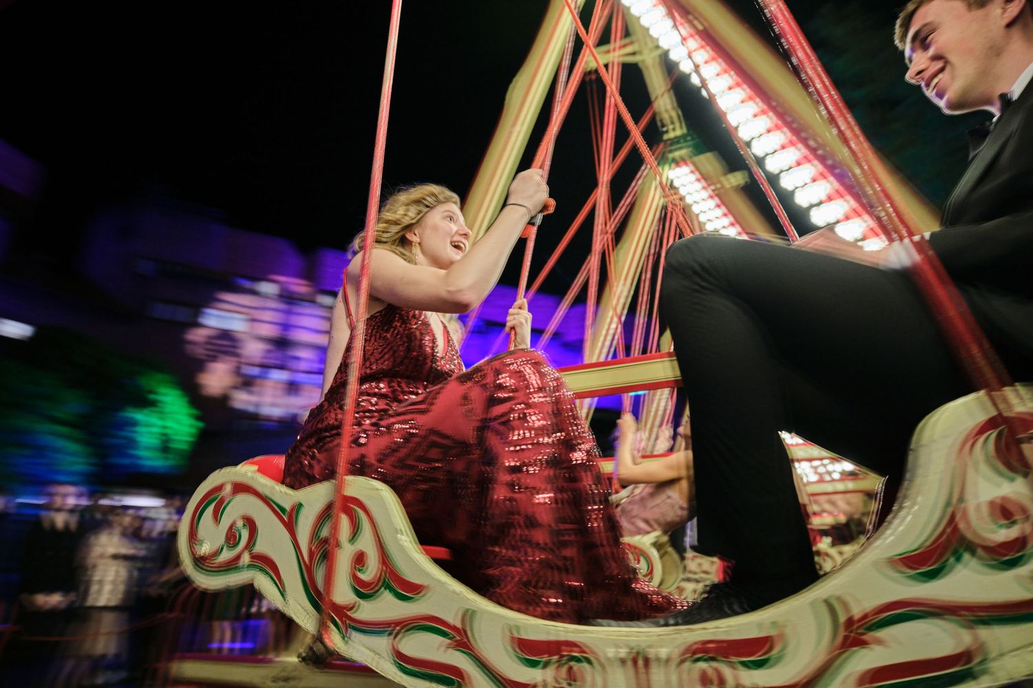 Carnival ride with glowing red lights creating motion trails in the dark.
