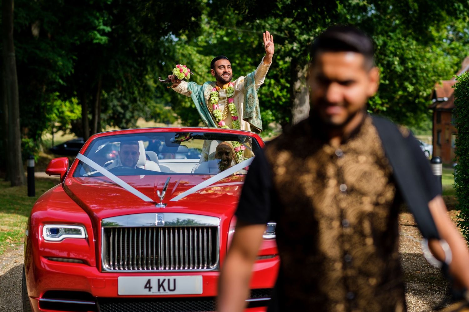 Luxury red Rolls Royce parked on a tree-lined driveway during a celebration.