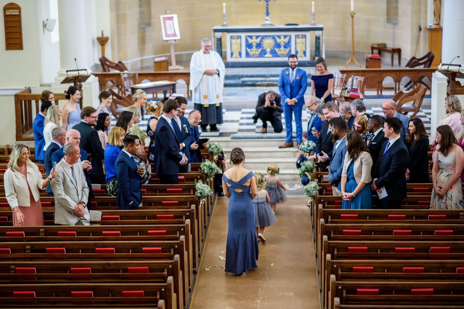 People gathered in church pews during a wedding ceremony with guests standing in the aisle.