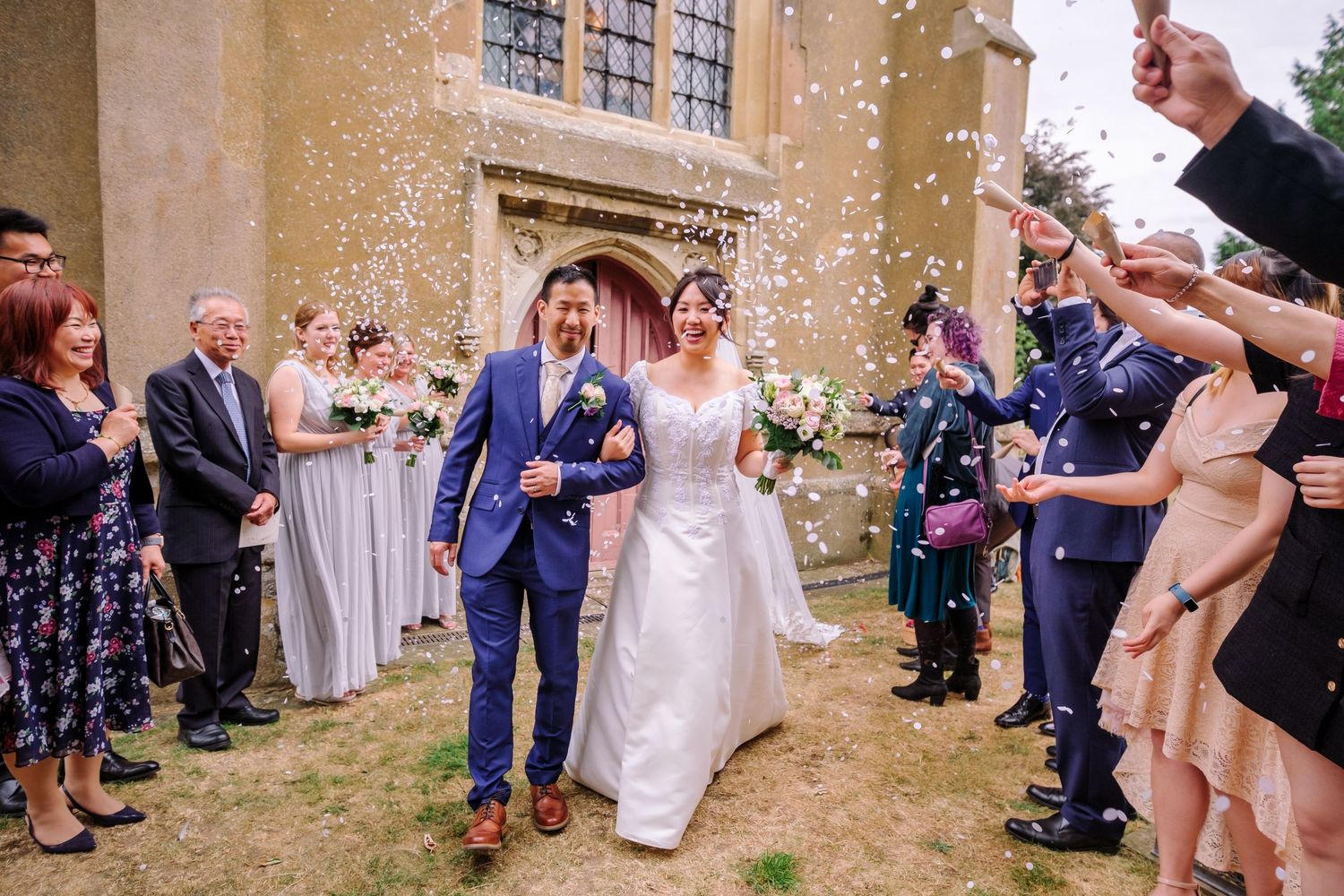 Wedding guests toss confetti outside a historic stone church during a joyful celebration.