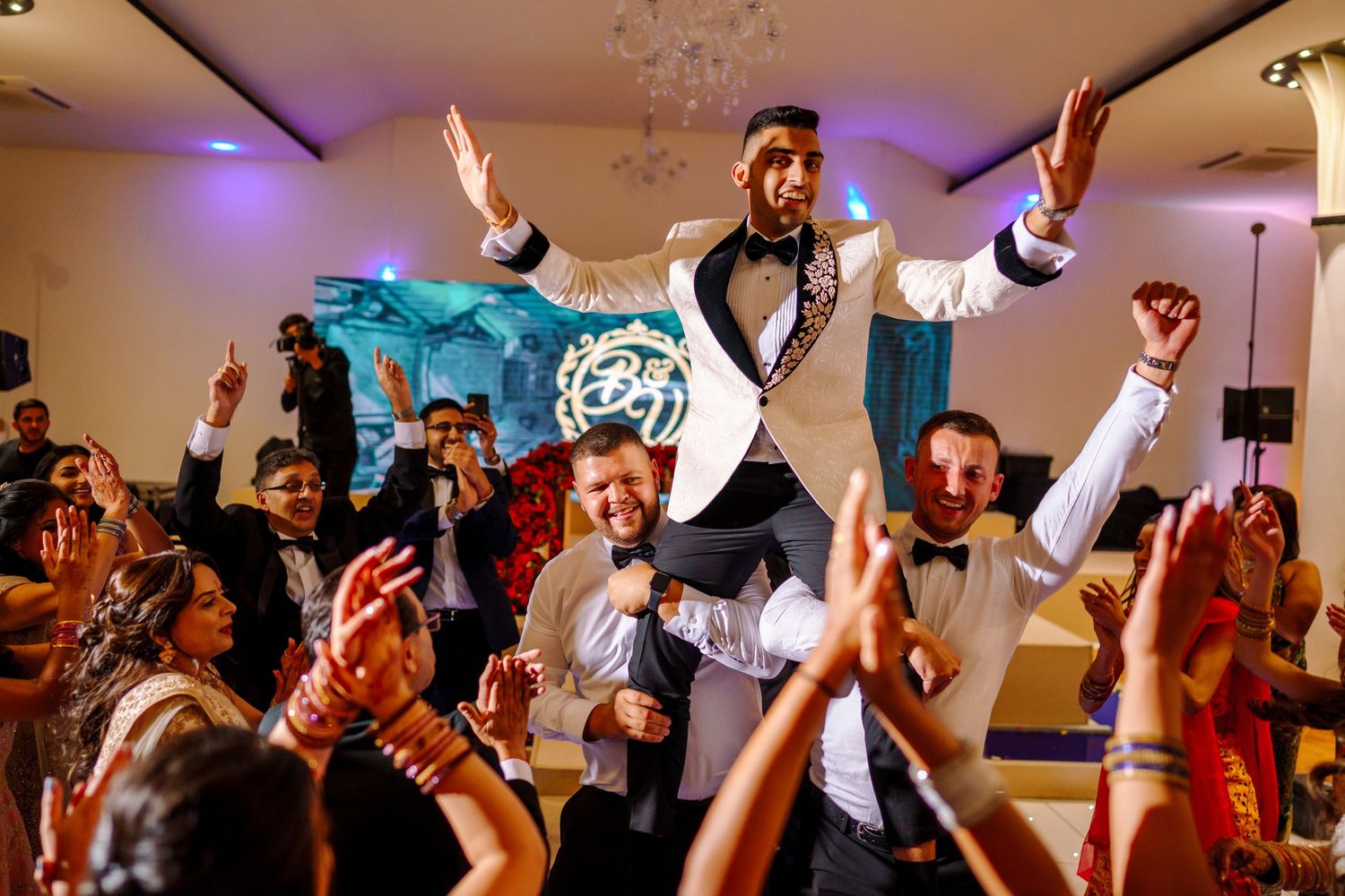 Wedding reception party with guests dancing and celebrating under purple lighting.