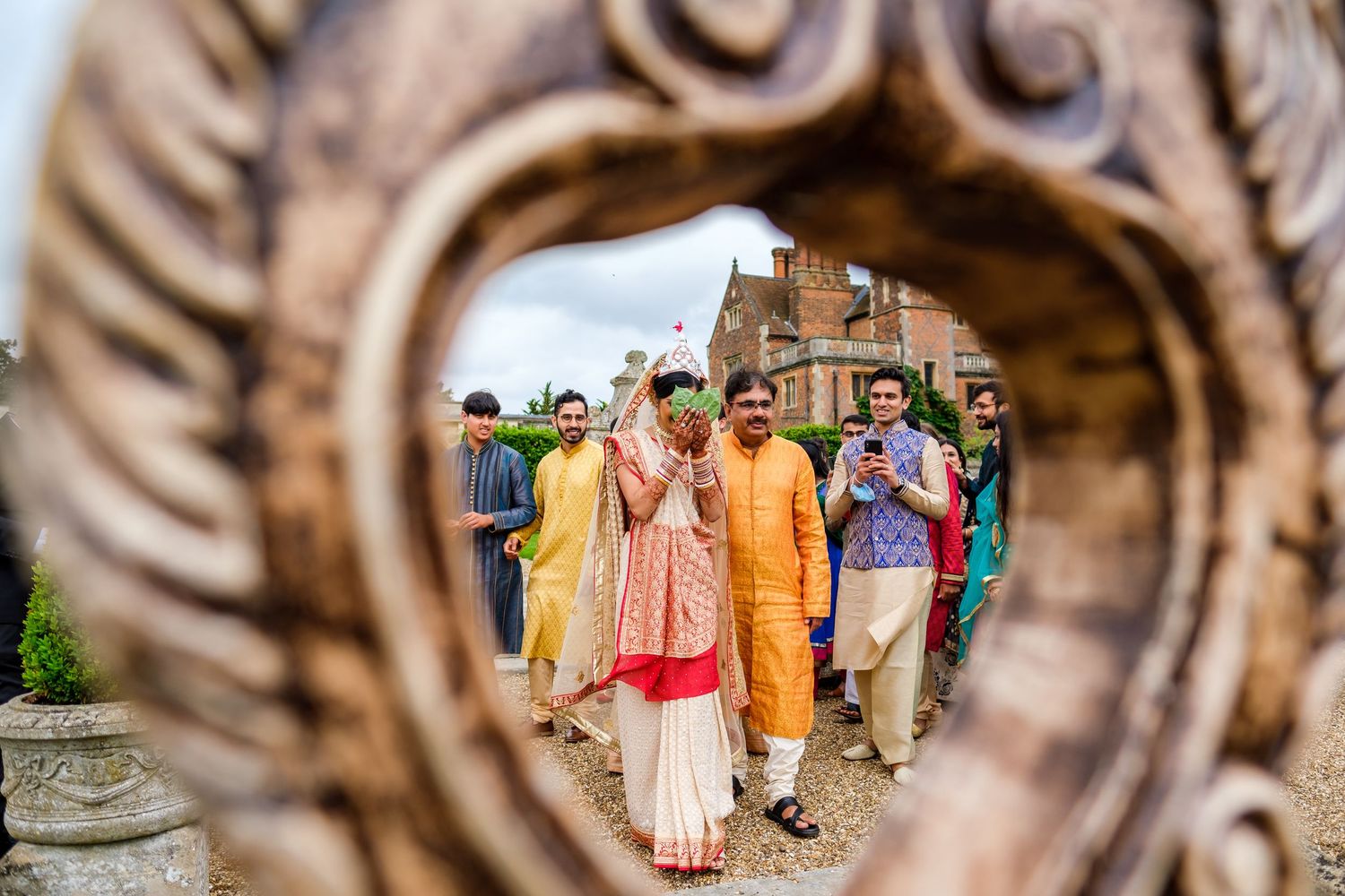 Colorfully dressed wedding guests gather in a garden setting with ornate architectural details.