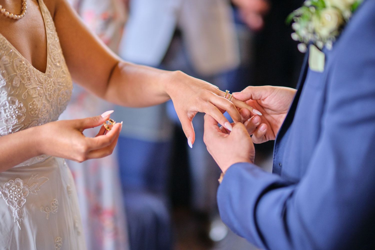 Close-up of hands during wedding ceremony exchange in formal attire.