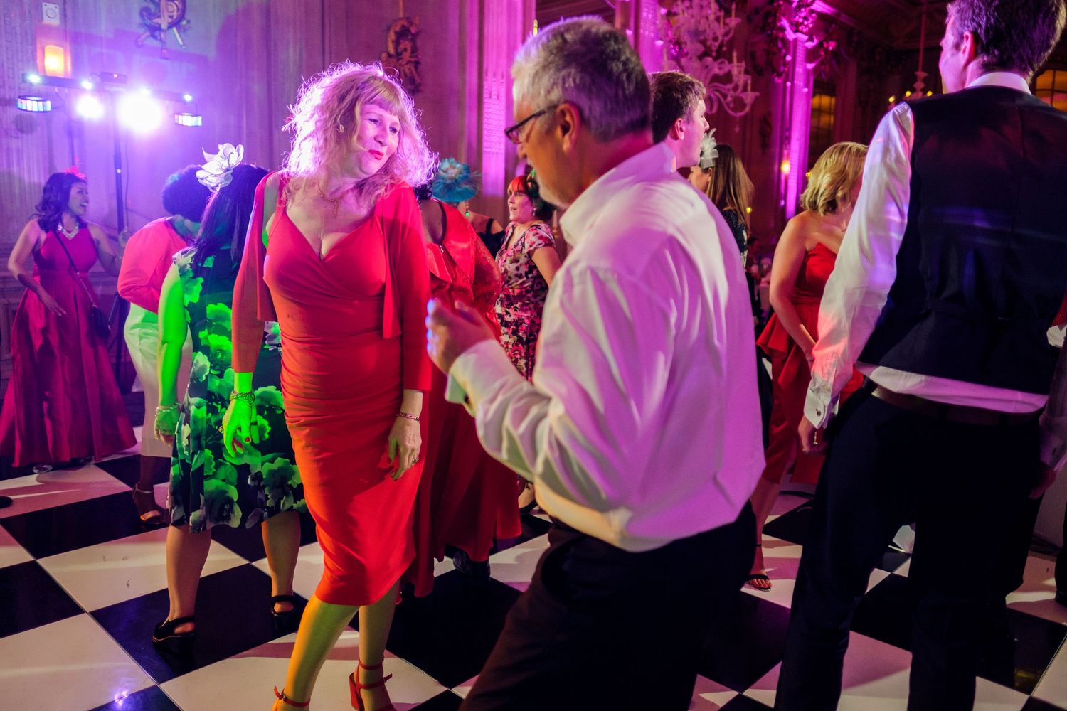 Wedding party dancing under vibrant purple lighting at an elegant reception venue.