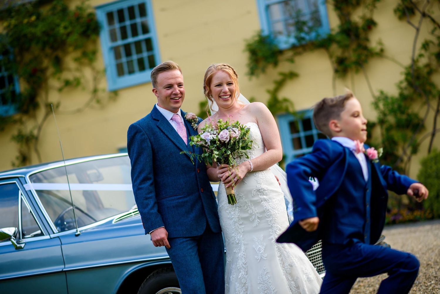 Wedding party poses outside yellow building with blue windows and climbing vines.