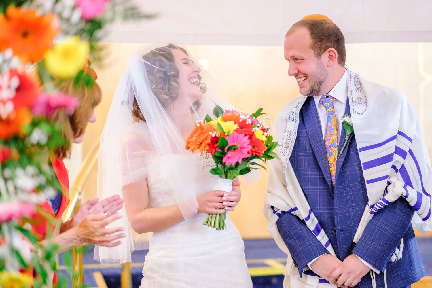 Wedding couple with bright orange and pink floral bouquet during ceremony.