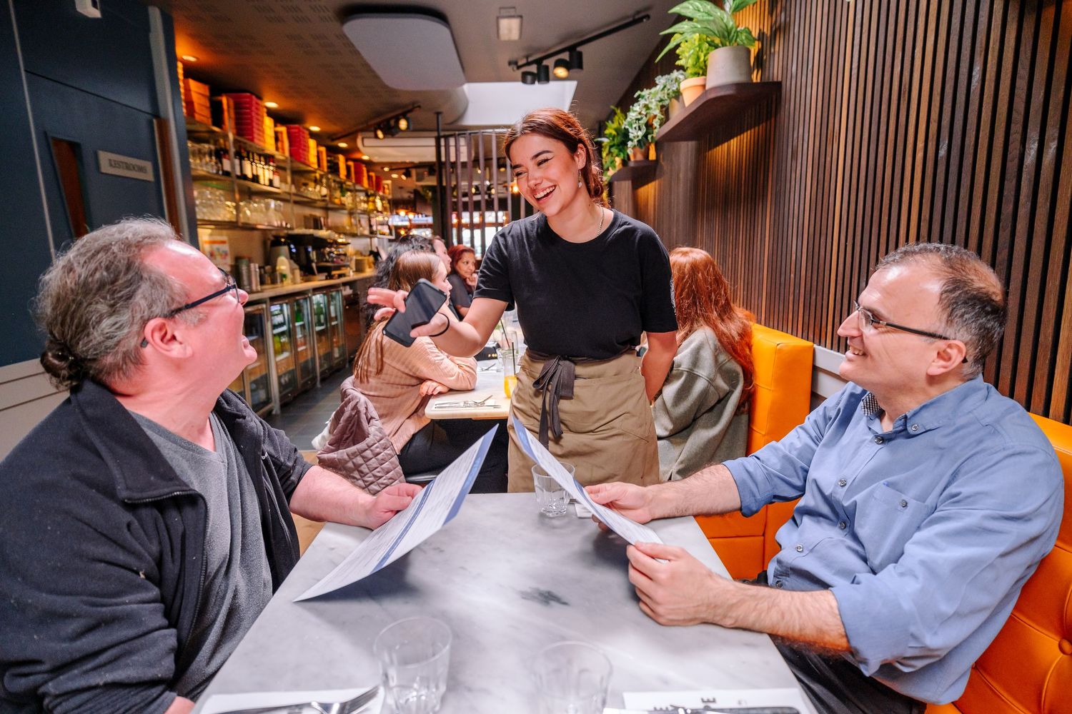 Diners engaged in conversation around tables in a modern restaurant setting.