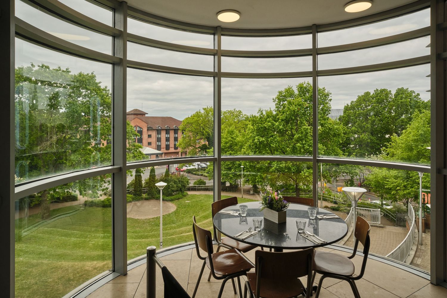 Curved panoramic windows offer scenic views of green landscaping from modern restaurant seating area.