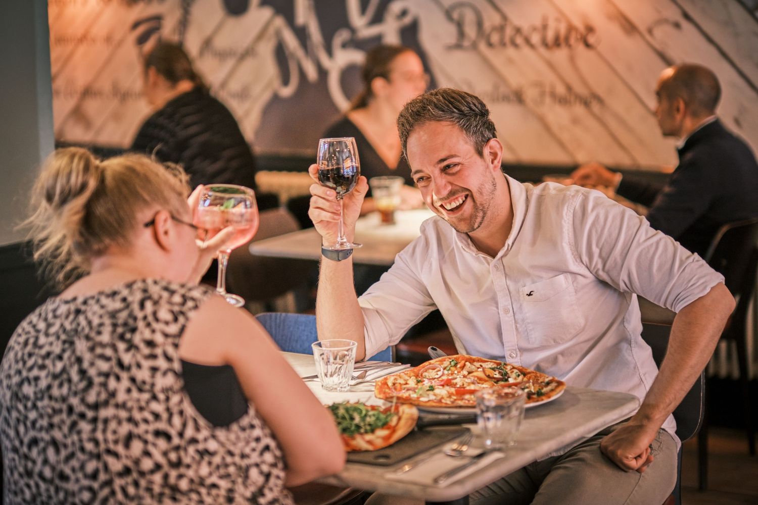 Diners sharing pizza and laughing together in a casual restaurant atmosphere.