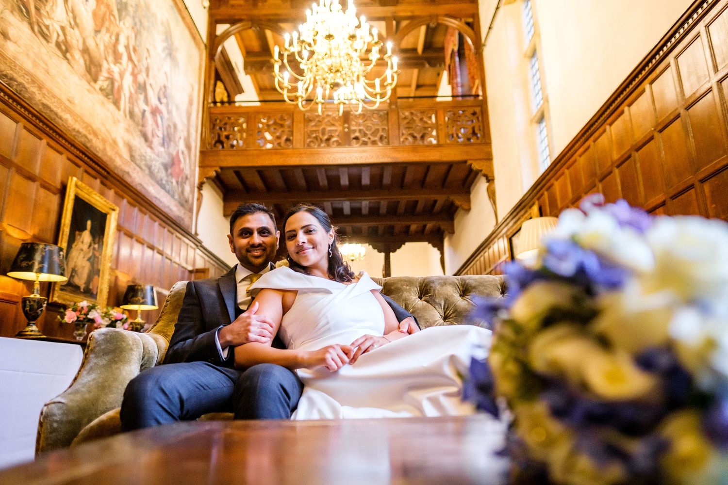 Couple poses romantically under elegant crystal chandeliers in an ornate ballroom setting.