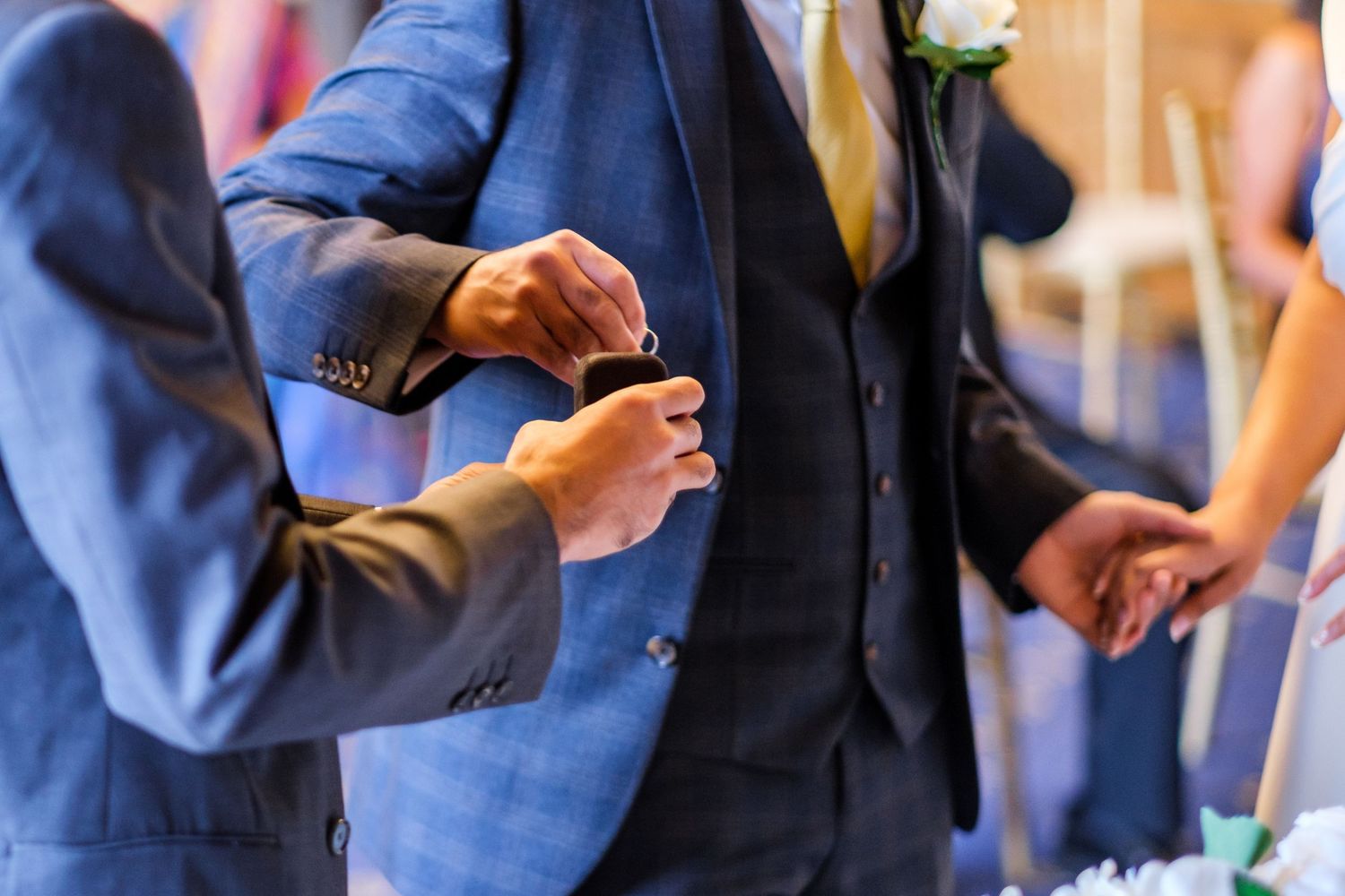 Wedding guests in navy blue suits gather together at a formal event with white rose boutonnieres.