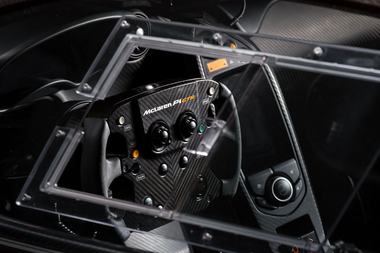 Close-up view of black carbon fiber racing car cockpit controls and steering wheel components.